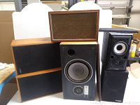 Front view showing five vintage speakers with wooden cabinetry and black grilles; one speaker grille removed showing drivers.