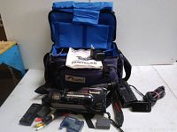 Yashica Finemovie8 camera recorder with Lowepro carrying bag and multiple accessories including remote, power adapter, cables, and batteries laid out on a white surface.