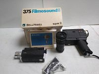 Wide shot of two vintage 8mm movie cameras, lens, accessories, and Belle & Howell box and manual.