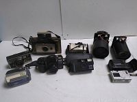 Wide view of the lot showing all cameras, lenses, camcorder, and cases placed on a white surface against a white backdrop