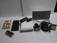 Lot showing Xbox 360 DVD drive, Bose iPod dock speaker, various remotes, alarm clock, and electrical components