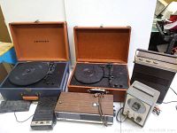 Two Crosley portable turntables in open leatherette cases with brown and blue exteriors. Also visible are additional vintage electronics including a speaker and cassette deck.
