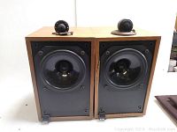 Front view of both speakers without grills showing midrange/bass drivers and separate tweeters placed on top.