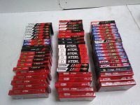 Photo shows multiple stacks of TDK blank audio cassette tapes in original packaging, arranged on a white surface.