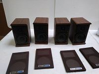 Four Koss M60 Plus bookshelf speakers shown without grills on white background. Wooden cabinets in wood grain finish. Front speaker drivers visible.
