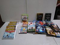 Wide view of all media items laid out on table against a white background, showing CDs, game cases, Blu-rays, and DVDs.