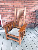 Angled side view of antique Mission style solid oak armchair with striped seat cushion showing wood grain and structure.