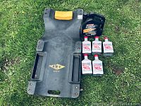 Photo showing black mechanics creeper dolly with yellow padded headrest and oil products on grass.