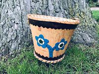 Front and side view of the cedar bark bucket showing blue floral design and zigzag painted patterns on the exterior.