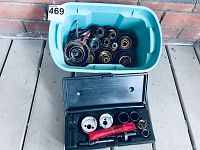 Photo showing blue plastic bin filled with multiple large core drill bits with serrated edges and a black plastic case containing core drill bits and accessories.