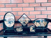 Five different shaped shadow boxes with cork carving scenes displayed on a black surface in front of a brick wall