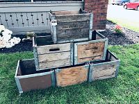 Stacked view of the six milk crates on grass outdoors, showing worn wood panels and metal framing with some repaired sections.