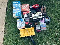 Overview photo showing all items laid on grass including staple guns in boxes, hardware caddy boxes, electrical tape, glue gun, hand planes, and organizer box