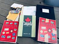 Overview of the stamp albums and envelopes showing two red Traveler Stamp Albums, a Canada and Provinces album, and a black binder with envelopes