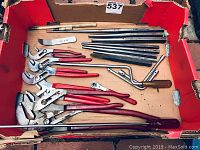 View of multiple hand tools including wrenches, pliers, pry bars, and chisels in a cardboard box