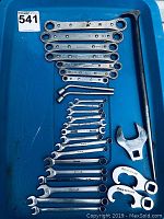 Top-down view of Snap-On wrenches arrayed on blue surface showing various sizes and types including combination and ratcheting models with two large specialty wrenches and chrome lever tool.