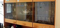 Cabinet with glass doors showing an array of china and glassware including plates, bowls, and decorative items.