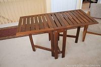 Full view of the wooden gate leg table showing slatted surface and fold-down leaves in extended position.