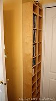 Side view of one Ikea laminated wood CD tower showing adjustable shelves and some DVDs and CDs stored inside.