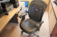 Black office chair with padded faux leather seat, mesh back, armrests and wheels from front angle