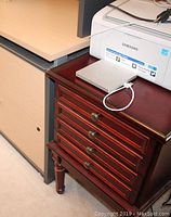 Mahogany side table next to a desk with items on top, showing drawer fronts and legs.