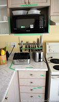 Kitchen countertop showing Panasonic microwave placed on a shelf with dishes on top, assorted kitchen knives on standby underneath, and an Oster toaster and Jasi roasting pan on the counter below with minor stains and wear evident.