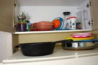 Shelf with three cast iron frying pans, plastic jugs and cups, and other kitchen items