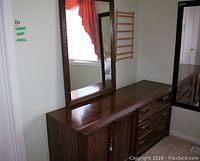 Wooden dresser showing the top surface, mirror, two doors on left, and drawers on right with brass handles. Visible wood grain and scratches on surface. One door knob is missing.