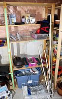 Wood shelving unit with assorted household items such as clay roaster, curtain rods, wire baskets, bins, ropes, flatware, and trays.