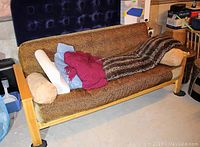 Full view of the wood-frame futon with cushions, pillows, and throws on top, showing the upholstery and frame style.