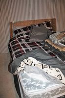 Queen bed with rattan metal framed headboard, plaid sheets, grey comforter and shams, additional bedding and throw pillows