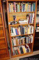 Wooden bookshelf filled with over 150 books of various sizes and colors, showing mixed collection of travel, fiction, and reference books.