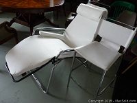 White faux leather adjustable lounge chair with padded armrests and headrest next to matching stool, both with chrome tubular steel frames.