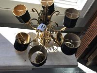 Top view of chandelier showing five black fabric lampshades and gold-tone curved metal arms with some visible damage to plastic light stems.