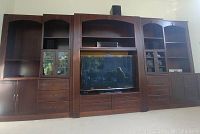 Full view of the entertainment unit assembled, showing central TV space, side cabinets with glass doors and drawers below, and open shelving on both ends. Dark wood with classic crown molding.