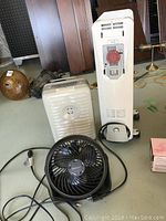 Three appliances on floor: De Longhi oil heater, small white heater, black Honeywell fan