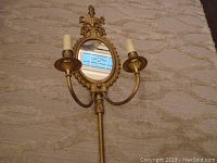 Brass wall sconce laying on carpet showing full front view with two candle-style lights and oval mirror.