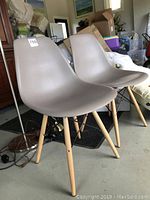 Two matching beige plastic seats with wooden legs chairs, showing side angle, table and room background.