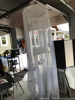 White princess-style canopy netting hanging in a garage, showing the full length of the netting reaching the ground.