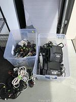 Two large plastic bins filled with assorted electronic accessories, including landline phones, remote controls, chargers, and cables.