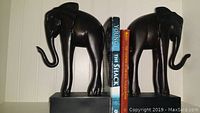 Pair of black elephant bookends holding books in place on shelf, view from front