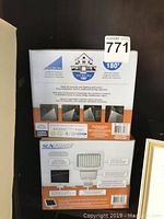 View of two Sunforce 100 LED solar motion activated lights in their original orange and white boxes showing product images and details.