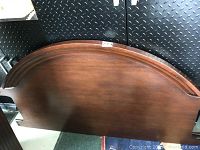 Curved wooden headboard of the bed frame, showing medium brown finish and arched top edge.