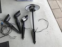 Four outdoor electric garden spotlights: three smaller and one larger Spotlight laid on gray concrete platform