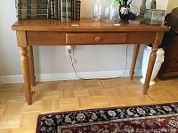 Side view of the wooden side table showing the front drawer and turned legs with minor nicks on top surface visible
