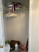 Closet with shelves containing party supplies, aluminum pans, gift bags stored above, beige wall and carpet floor.