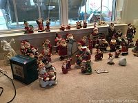 Wide view of most Christmas Santa Claus figurines arranged on floor with some holiday decor and music box on the left.
