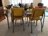 View of the table and three yellow vinyl chairs from behind showing metal legs and the condition of seats and backs.