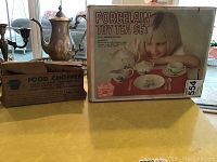 Photo showing the Keystone manual food chopper box next to the porcelain toy tea set box with a child pictured on it.