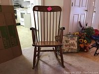 Full front view of wooden rocking chair with vertical slat backrest, loose arms, and worn finish.